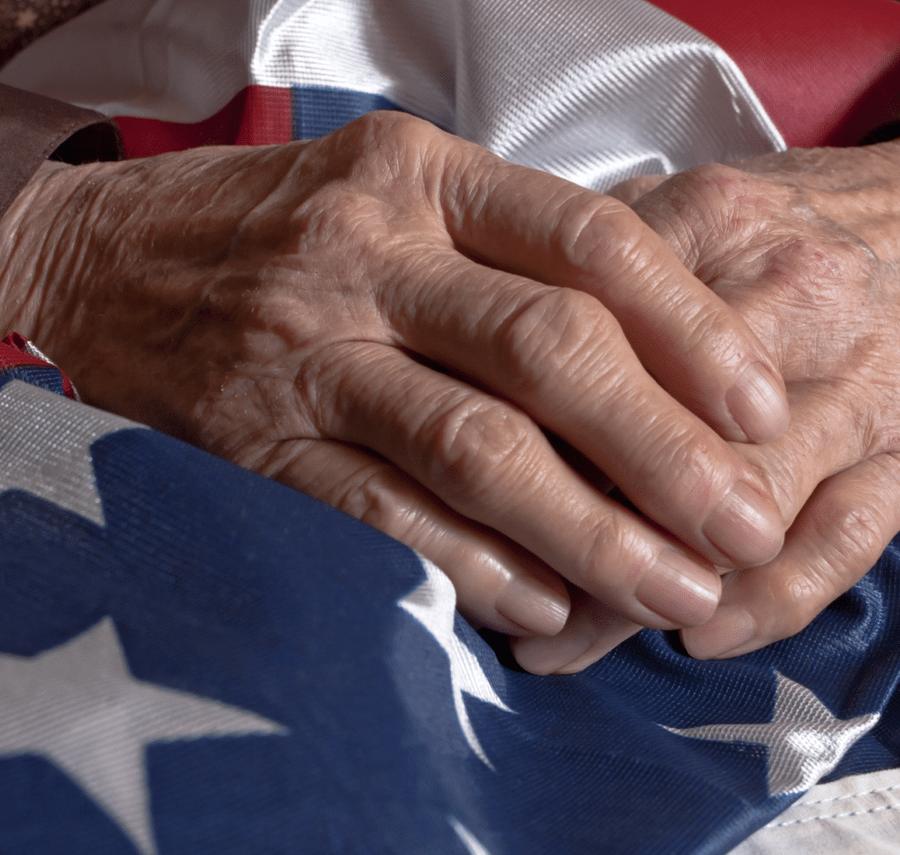 An older veteran's hands resting on an American flag